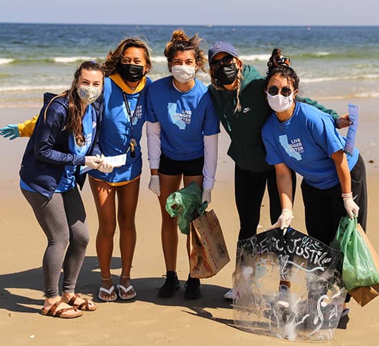 Five women holding trash bags at a beach cleanup